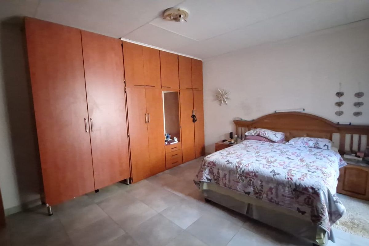 A spacious bedroom featuring extensive built-in wooden cupboards and tiled flooring, offering a functional layout with ample storage space.