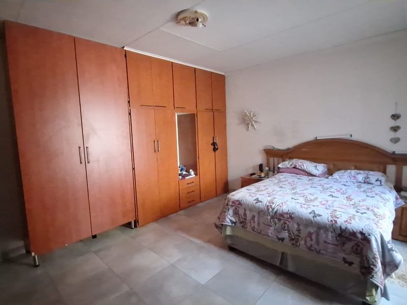A spacious bedroom featuring extensive built-in wooden cupboards and tiled flooring, offering a functional layout with ample storage space.