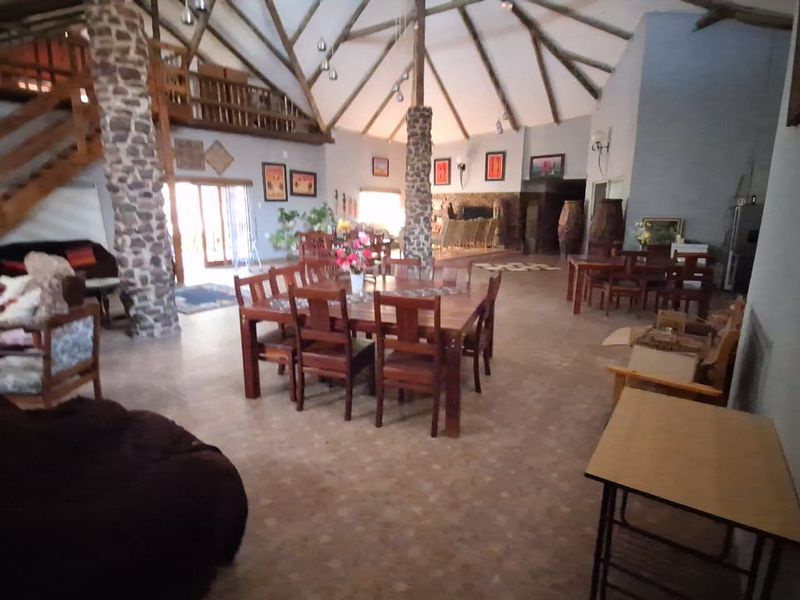 Spacious open-plan living and dining area featuring high vaulted ceilings with exposed timber trusses, stone columns, and a mezzanine level.