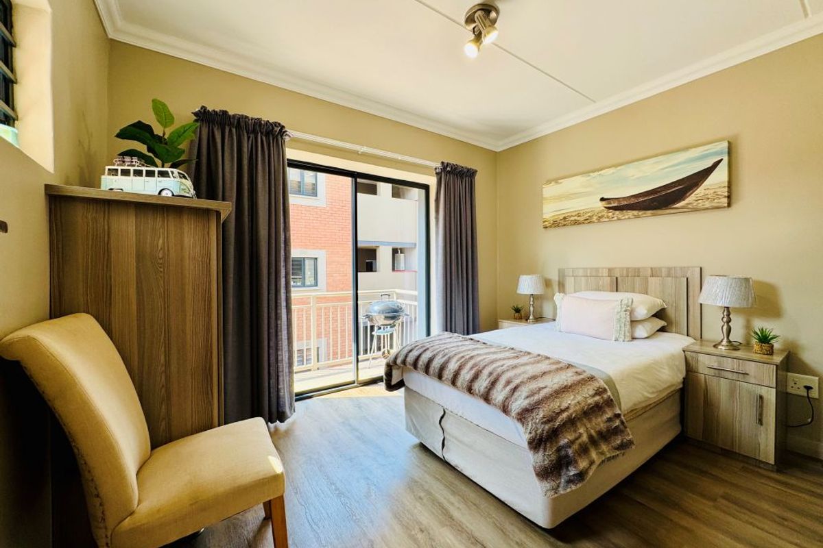 A well-maintained bedroom featuring laminate flooring, neutral walls, and a sliding glass door providing access to a private balcony.