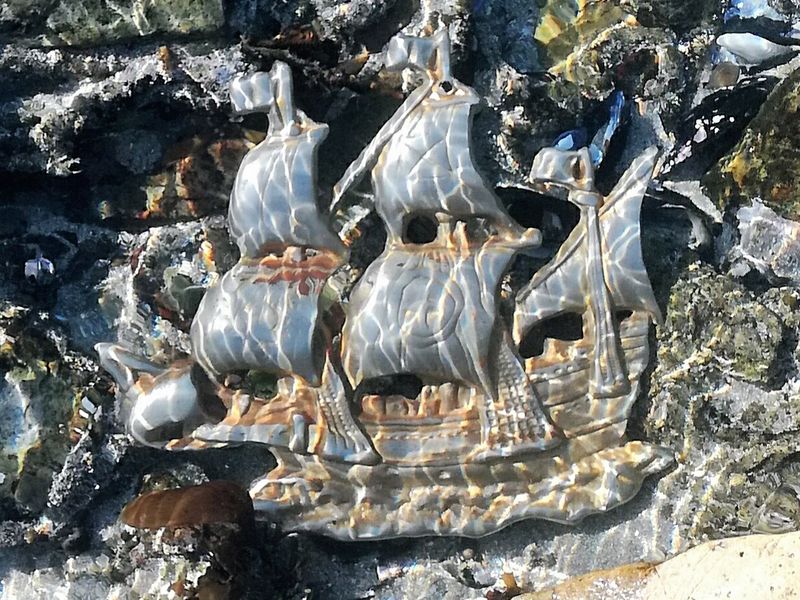 A close-up view of a decorative metal ship ornament embedded in a textured stone surface.