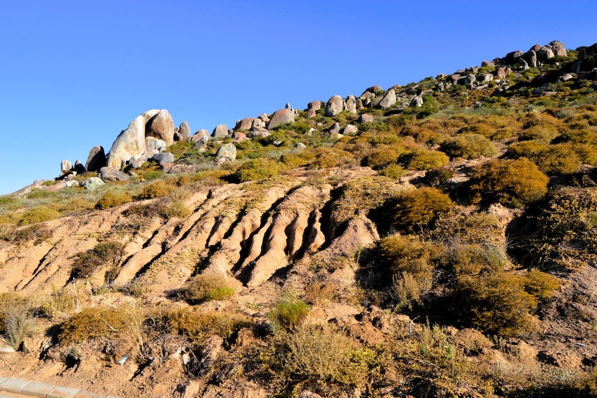 A view of the sloped, natural terrain featuring native vegetation and prominent rock formations on the vacant residential land.