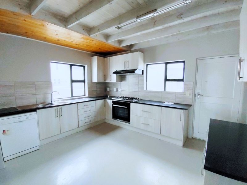 A clean, functional kitchen featuring light-toned cabinetry, dark countertops, built-in cooking appliances, and exposed timber ceiling beams.