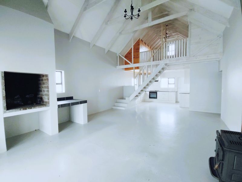Spacious open-plan living area featuring a vaulted ceiling with exposed trusses, a mezzanine level, built-in fireplace, and a functional kitchen with integrated appliances.