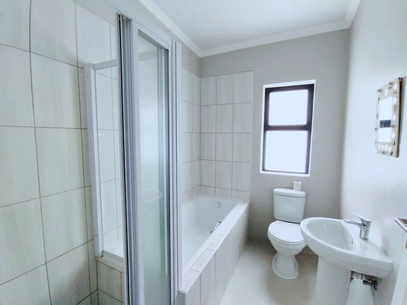 A clean, modern bathroom featuring a built-in bathtub, separate shower enclosure, pedestal basin, and toilet with neutral wall tiling.
