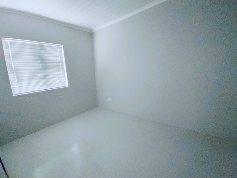 A clean, empty bedroom featuring neutral tiled flooring, coved ceilings, and fitted venetian blinds, offering a blank canvas for personalization.