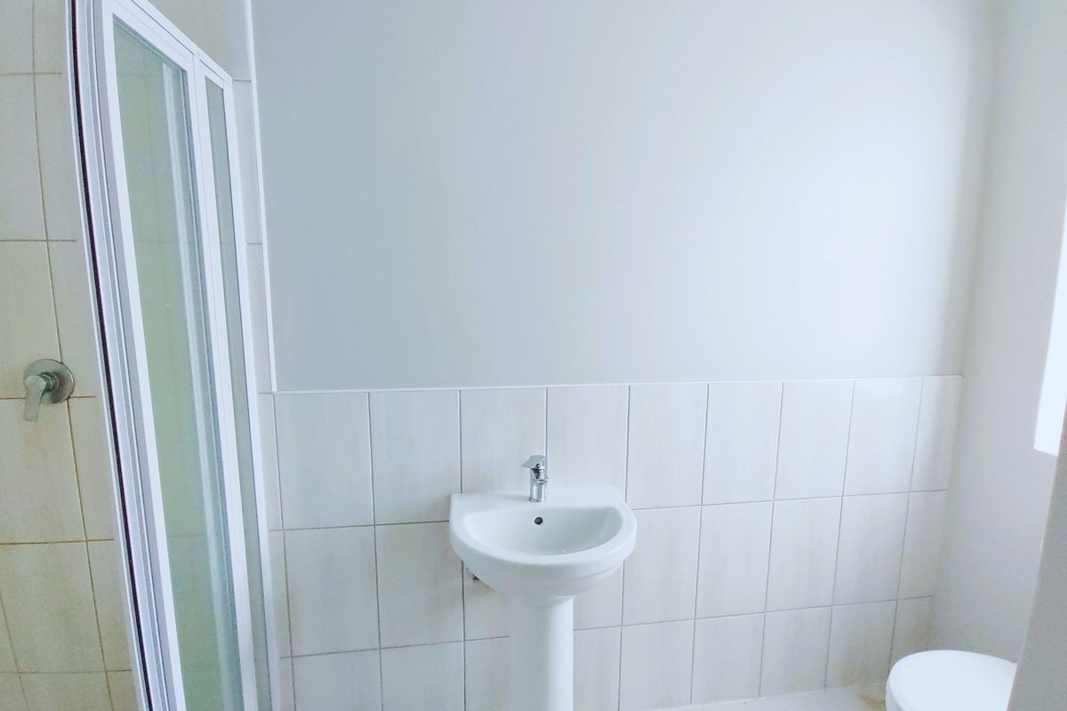 A clean, minimalist bathroom featuring a pedestal basin, a shower enclosure, and a toilet with neutral wall tiling.