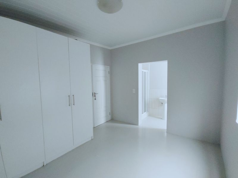 A clean, neutral bedroom featuring built-in cupboards and direct access to an en-suite bathroom.