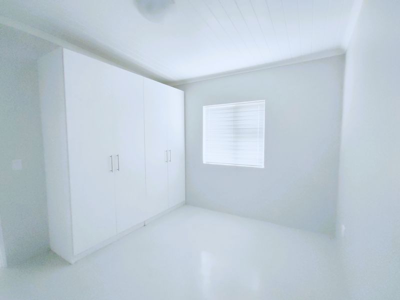 A bright, empty bedroom featuring clean white walls, built-in cupboards, and a classic tongue and groove ceiling.