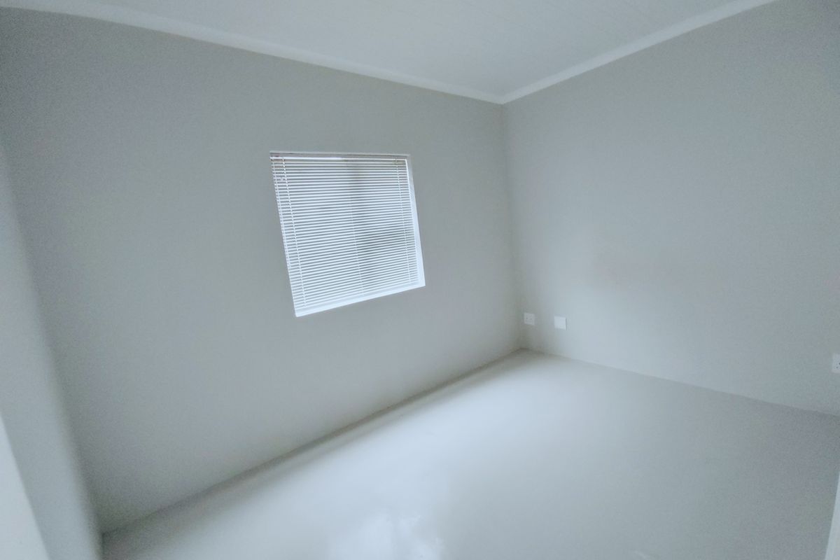 A clean, empty bedroom featuring neutral walls, a single window with fitted venetian blinds, and smooth flooring.