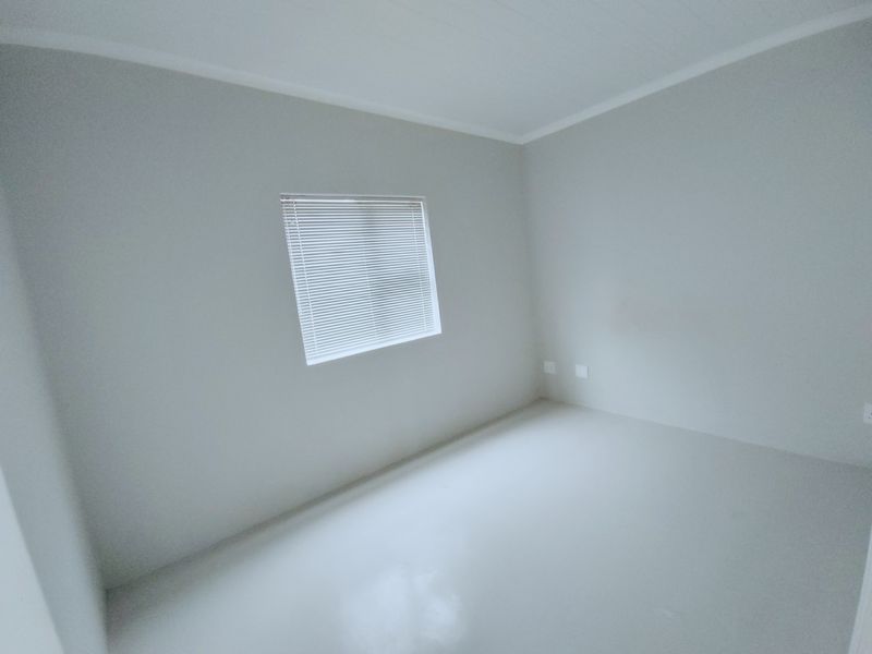 A clean, empty bedroom featuring neutral walls, a single window with fitted venetian blinds, and smooth flooring.
