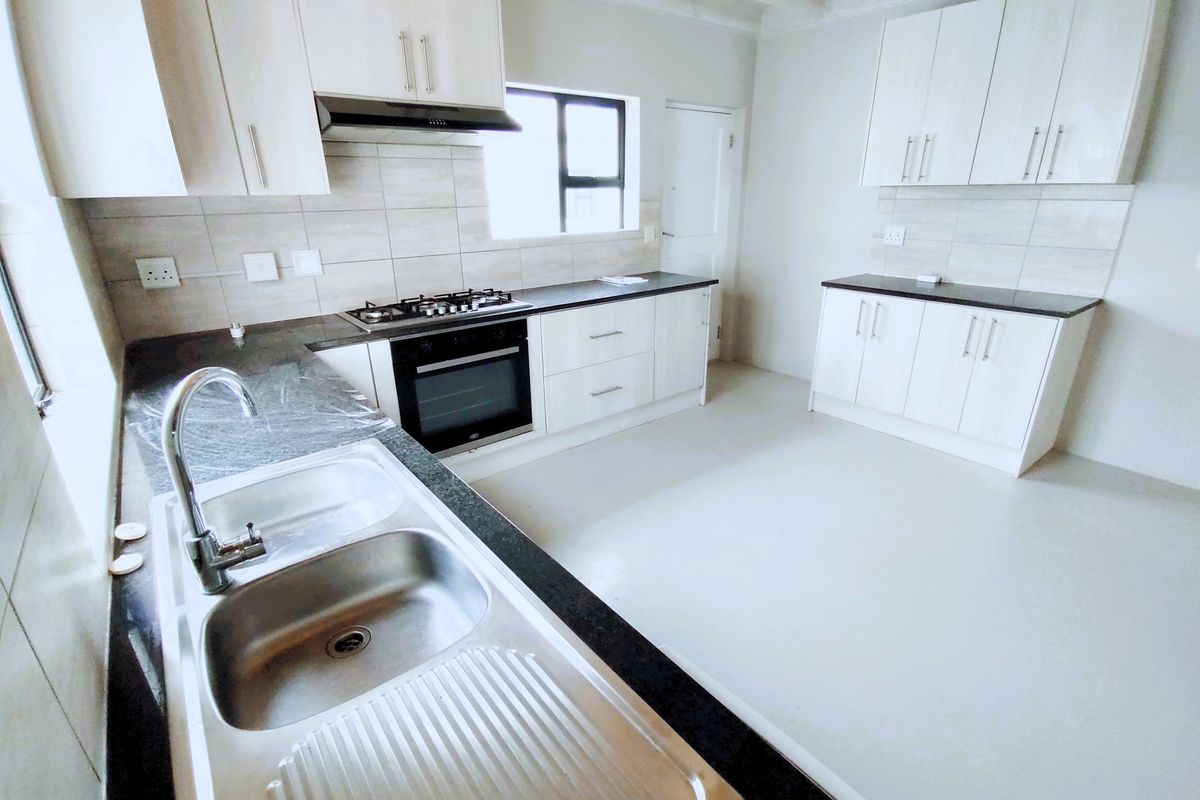 A clean, modern kitchen featuring white cabinetry, dark granite countertops, a gas hob, built-in oven, and a stainless steel double sink.