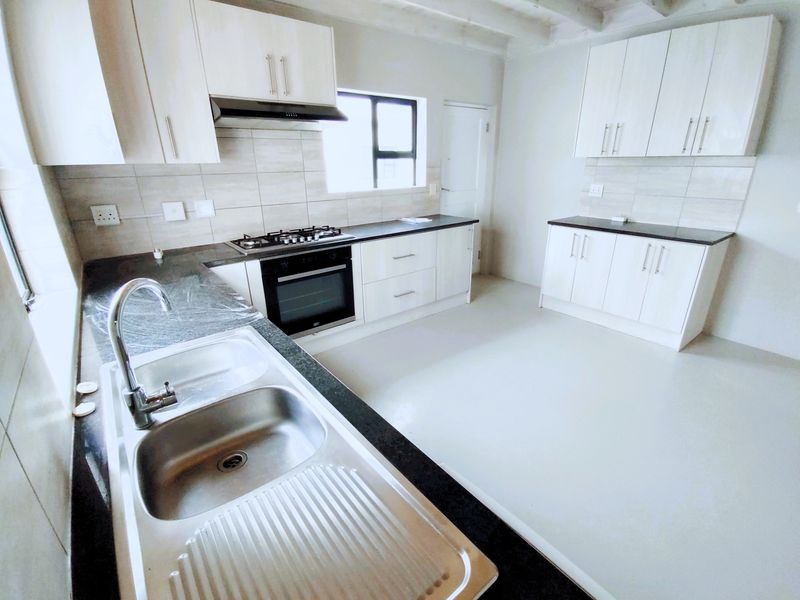 A clean, modern kitchen featuring white cabinetry, dark granite countertops, a gas hob, built-in oven, and a stainless steel double sink.
