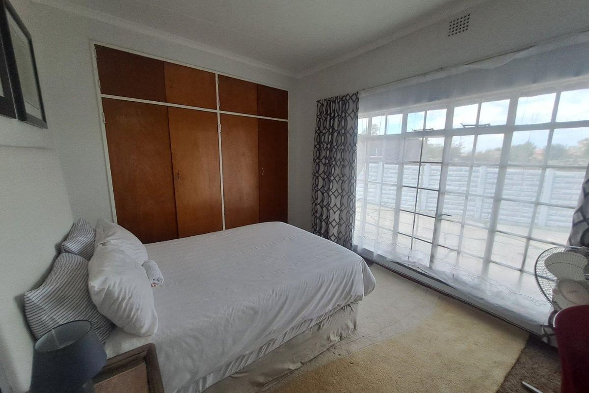 A bedroom featuring built-in wooden cupboards and a large sliding glass door providing access to the exterior.