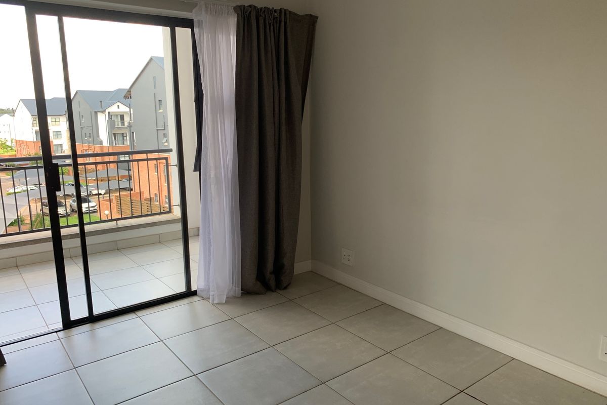 A bright, empty living area featuring neutral tiled flooring and a large sliding glass door providing access to a private balcony.