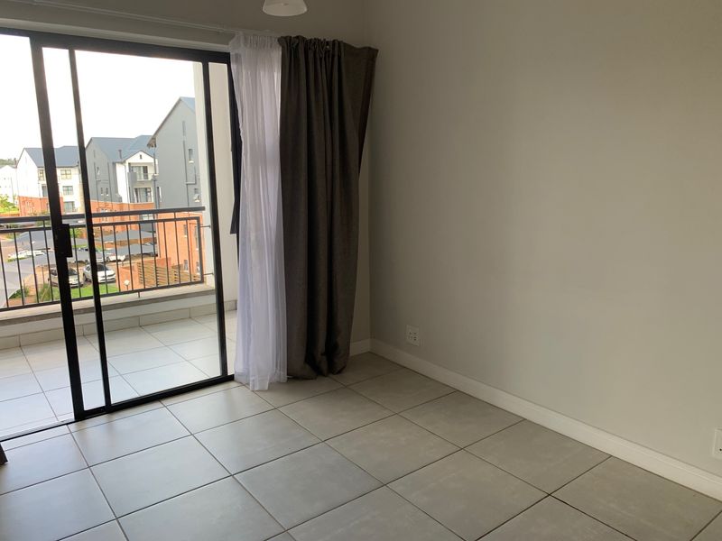 A bright, empty living area featuring neutral tiled flooring and a large sliding glass door providing access to a private balcony.