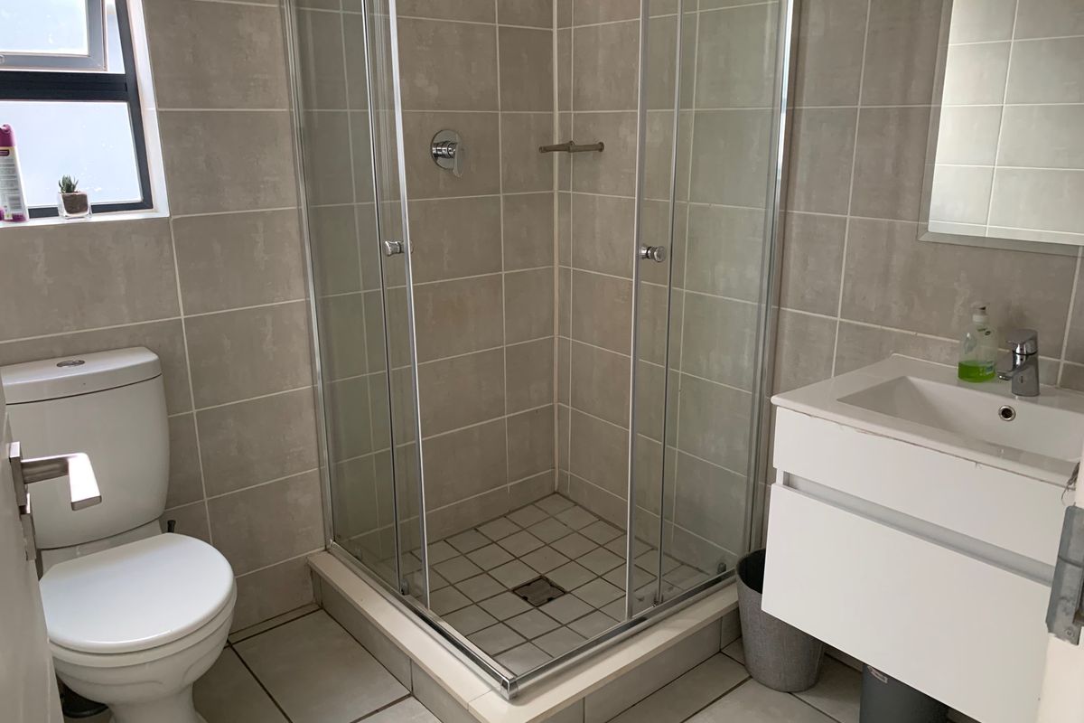 A clean, modern bathroom featuring a glass shower enclosure, wall-mounted vanity with basin, and neutral floor-to-ceiling tiling.