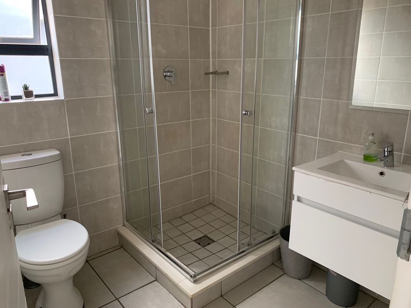 A clean, modern bathroom featuring a glass shower enclosure, wall-mounted vanity with basin, and neutral floor-to-ceiling tiling.