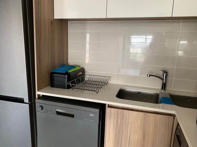 Modern kitchen area featuring sleek wood-grain cabinetry, stone countertops, a stainless steel sink, and a subway tile backsplash.