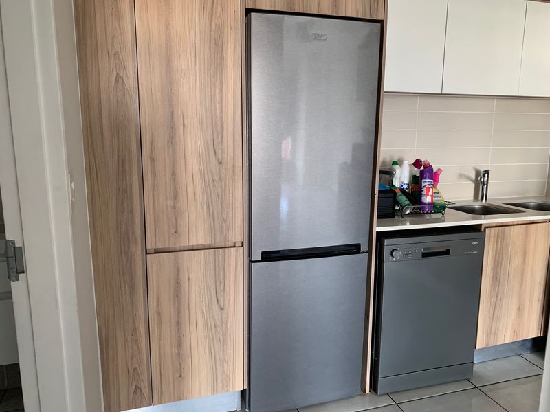 Modern kitchen featuring wood-grain cabinetry, a stainless steel sink, tiled backsplash, and integrated appliance space.