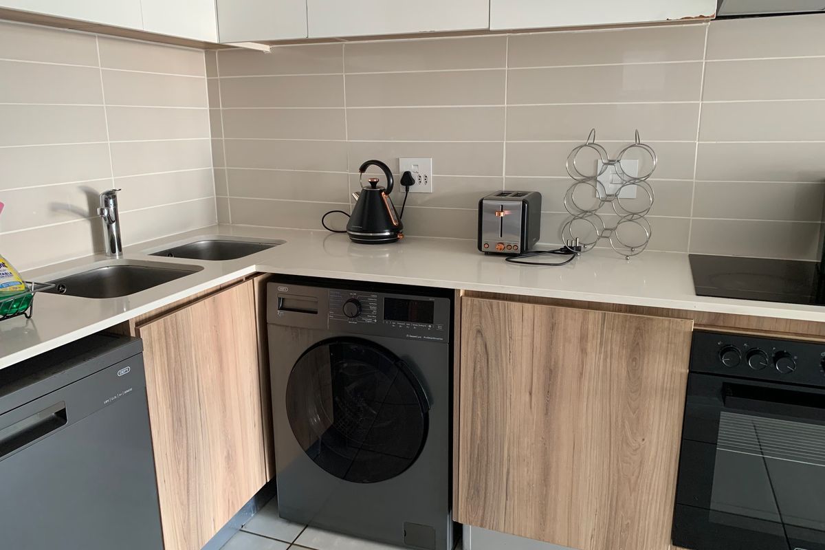 Modern kitchen featuring wood-grain cabinetry, stone countertops, integrated washing machine, built-in oven, and hob with a clean tiled backsplash.