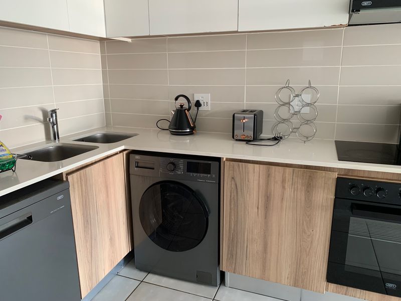 Modern kitchen featuring wood-grain cabinetry, stone countertops, integrated washing machine, built-in oven, and hob with a clean tiled backsplash.