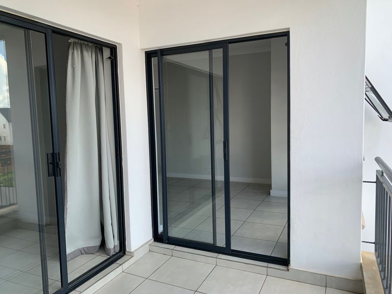 A clean, tiled balcony area featuring modern black-framed sliding glass doors providing access to the interior living space.