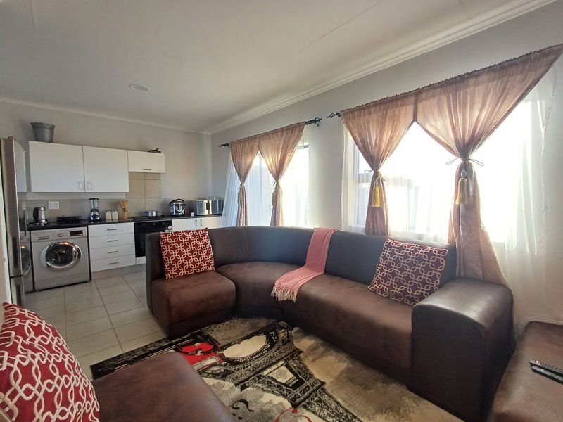 Open-plan living area featuring a compact kitchen with built-in cabinetry, integrated appliances, and tiled flooring, seamlessly connected to the lounge space.