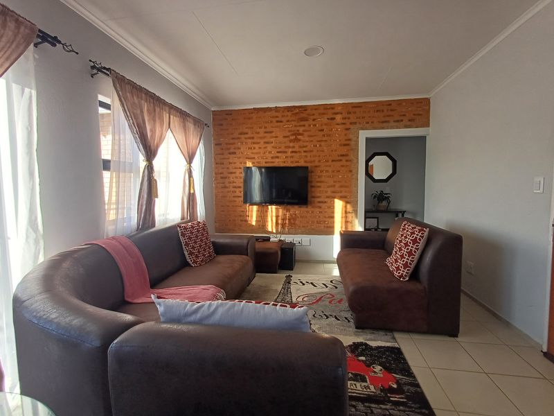 A living room featuring an exposed brick accent wall, tiled flooring, and recessed ceiling lighting, providing a warm and textured living space.