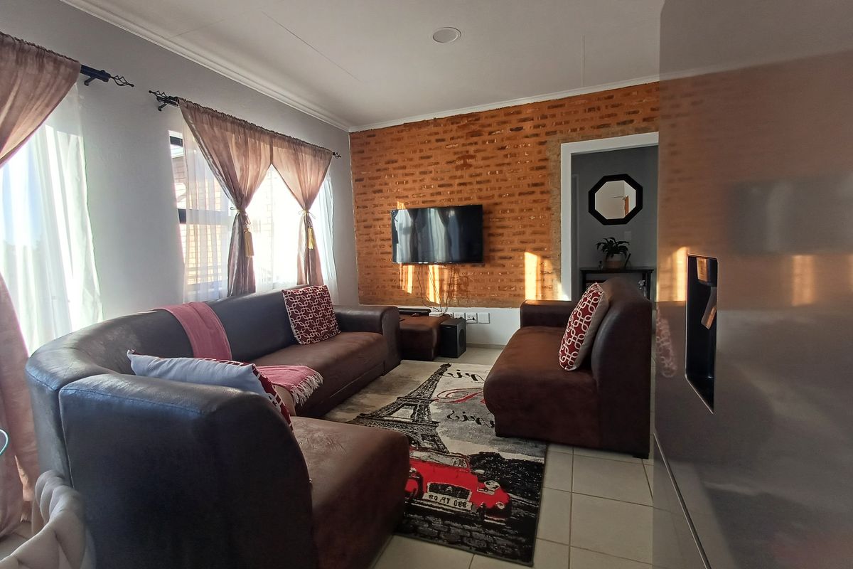 A cozy living room featuring an exposed brick accent wall, tiled flooring, and recessed ceiling lighting, creating a warm and inviting atmosphere.
