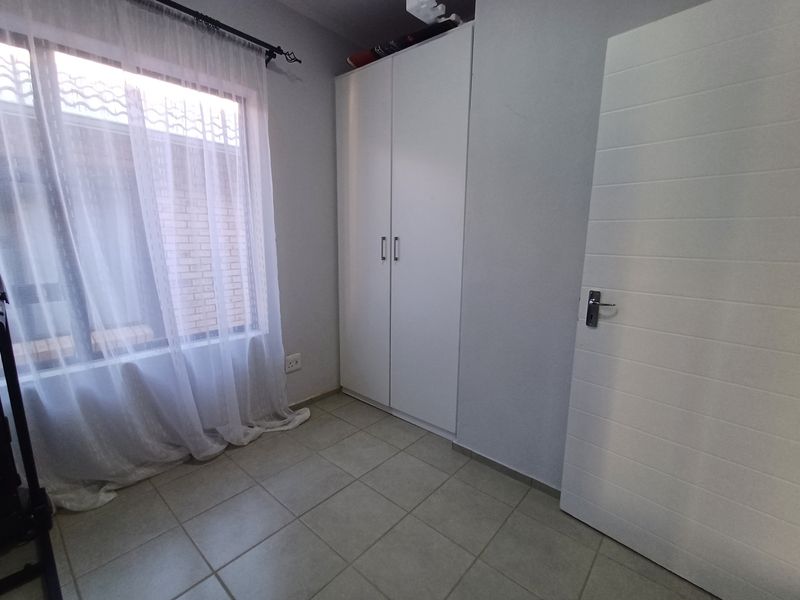 A clean, empty bedroom featuring neutral tiled flooring, a built-in white wardrobe, and natural light from the window.