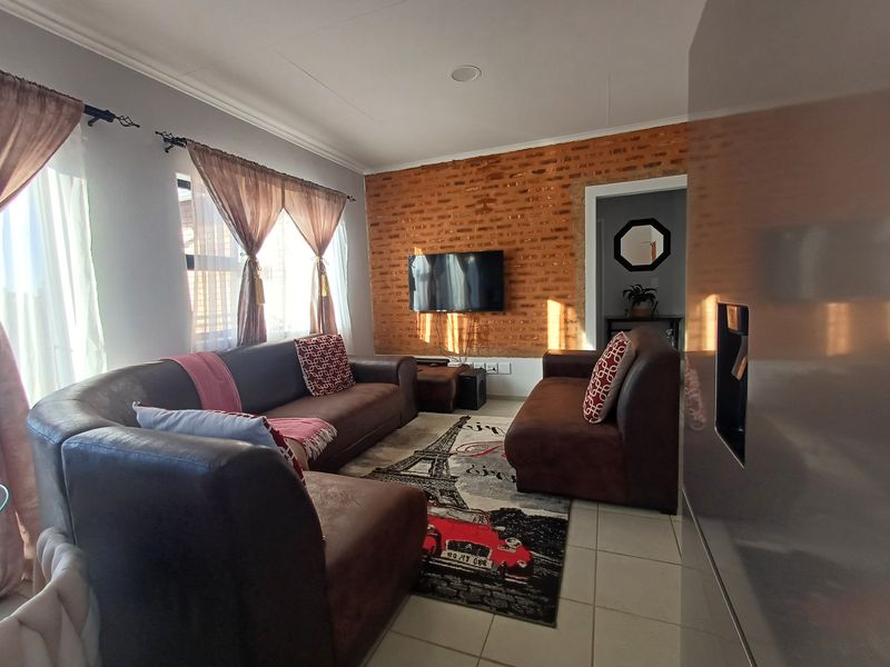 A cozy living room featuring an exposed brick accent wall, tiled flooring, and recessed ceiling lighting, creating a warm and inviting atmosphere.