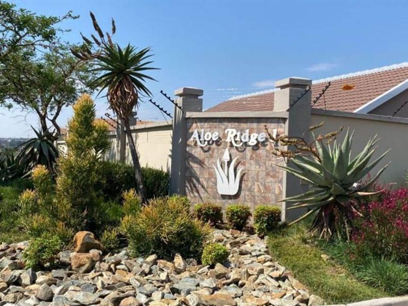 The entrance to Aloe Ridge 1 featuring a stone-clad signage wall, electric fencing, and well-maintained landscaped gardens.