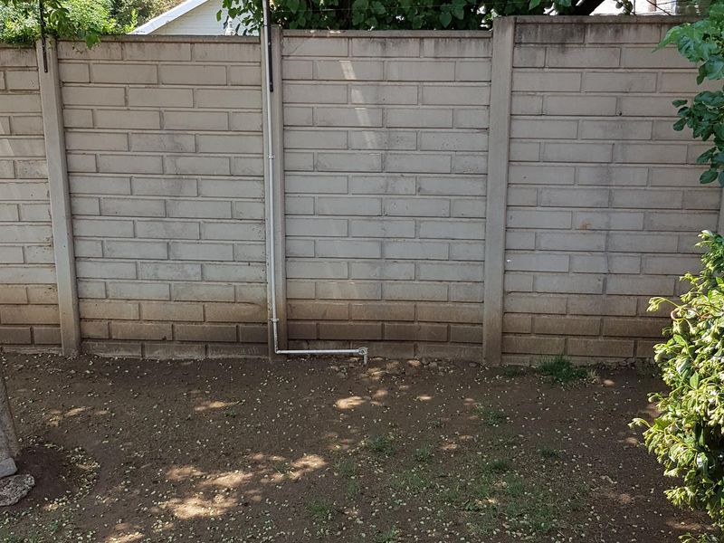 A rear garden area featuring a paved patio, timber pergola, and a precast concrete boundary wall, currently requiring landscaping and lawn maintenance.