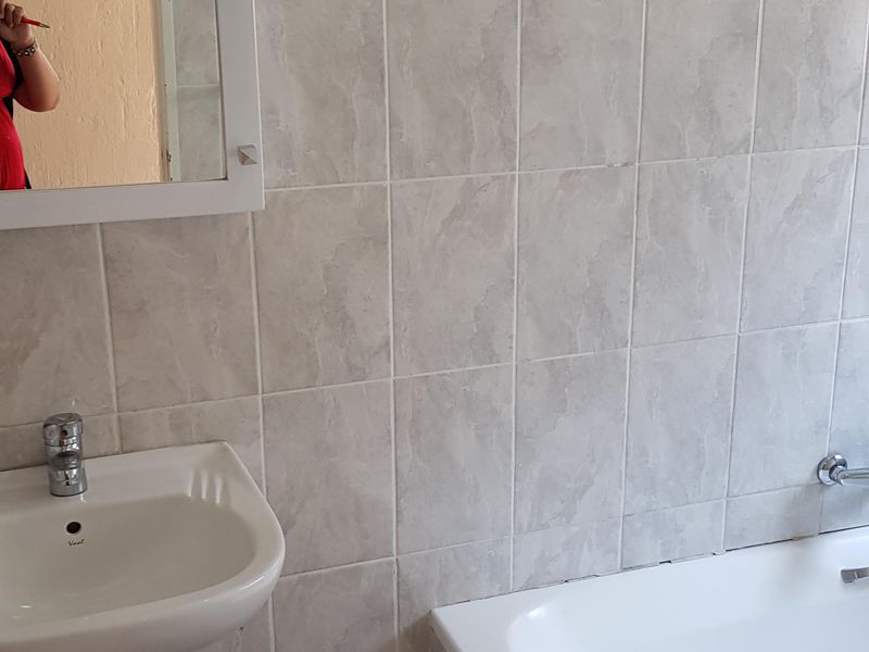 A functional bathroom featuring a pedestal basin, bathtub, and neutral wall tiling. The space is clean and ready for potential cosmetic updates.