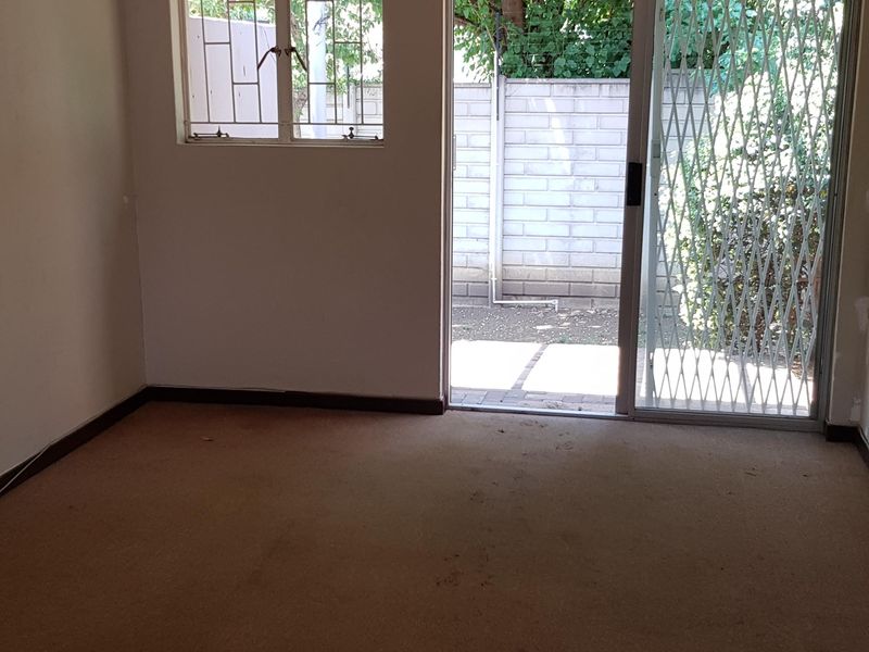 An empty living room featuring carpeted flooring, a ceiling light, and a sliding glass door with a security gate leading to an outdoor area.