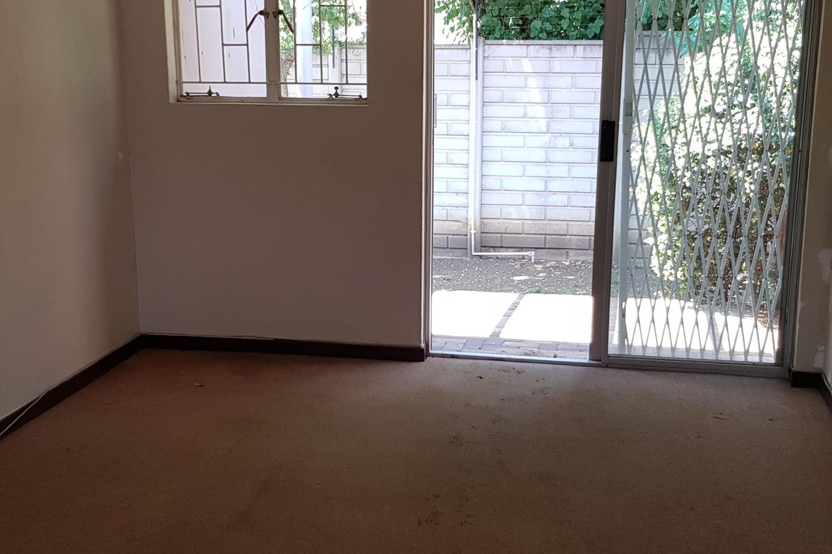 An empty living room featuring carpeted flooring, a ceiling light, and a sliding glass door with a security gate leading to an outdoor area.