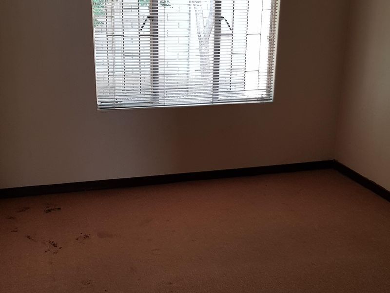 An empty bedroom featuring a window with security bars, venetian blinds, and a curtain rod, requiring carpet replacement or professional cleaning.