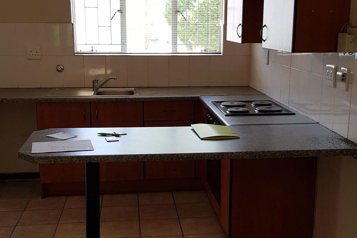 Functional kitchen featuring laminate cabinetry, built-in electric hob, stainless steel sink, and tiled splashback with a breakfast bar extension.