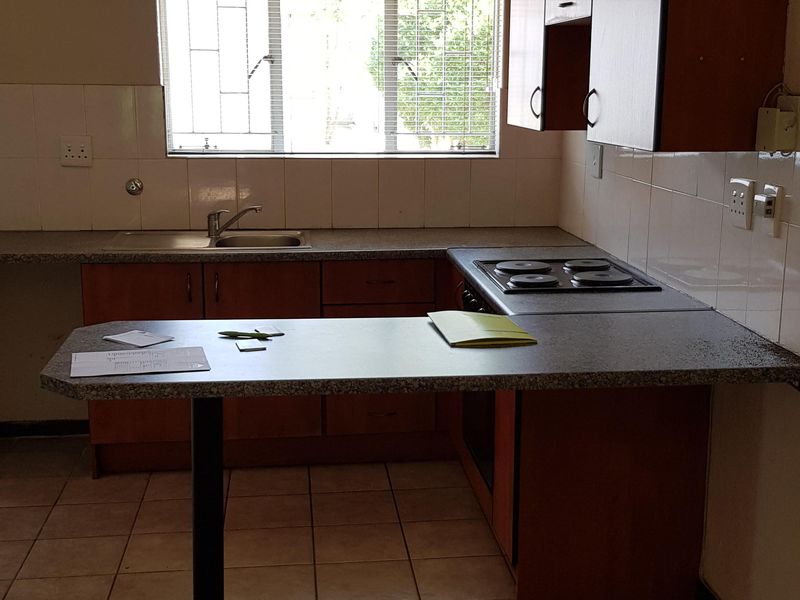 Functional kitchen featuring laminate cabinetry, built-in electric hob, stainless steel sink, and tiled splashback with a breakfast bar extension.