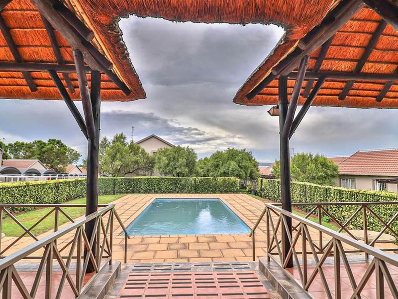 Outdoor pool area featuring a thatched gazebo, paved decking, and perimeter hedging, providing a communal recreational space within the apartment complex.