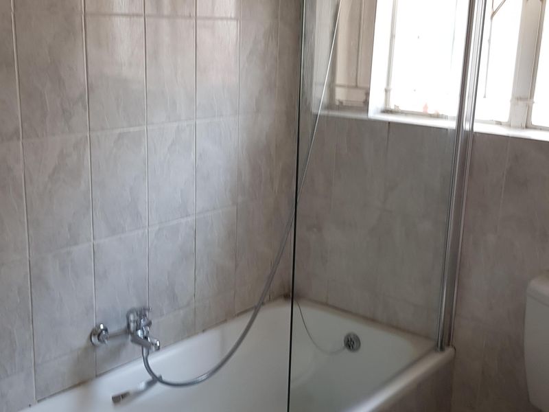 A functional bathroom featuring a bathtub with a glass shower screen, ceramic wall and floor tiling, and a standard toilet.