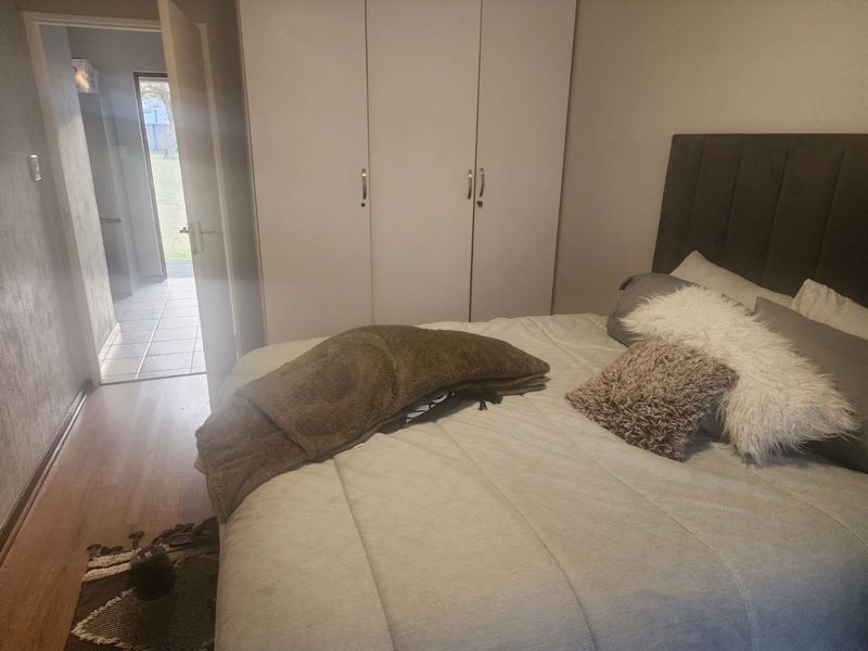 A bedroom featuring built-in cupboards and laminate flooring, with a view leading into an adjacent tiled hallway.