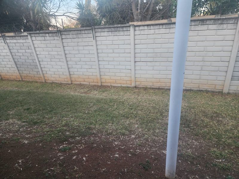 A private rear garden area featuring a concrete block boundary wall topped with security razor wire and a grass lawn.