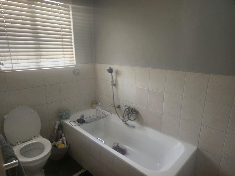 A functional bathroom featuring a bathtub with a shower mixer, a toilet, and tiled wall finishes with venetian blinds.