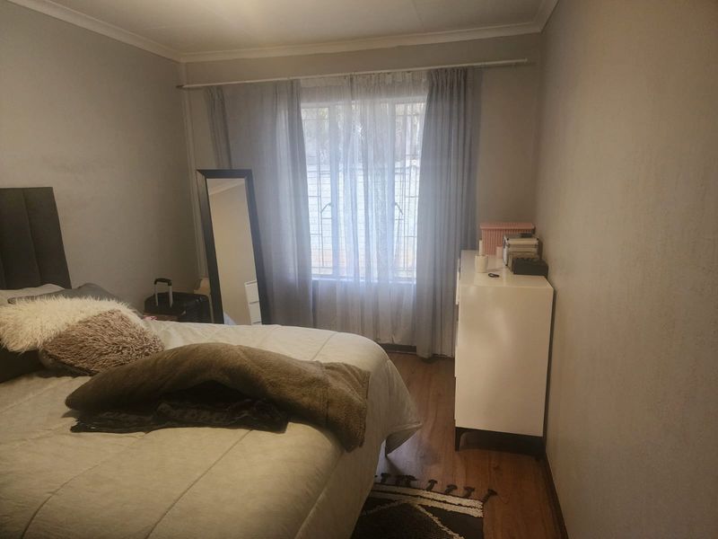 A standard bedroom featuring laminate flooring, neutral wall tones, and a window fitted with security bars and curtain rods.