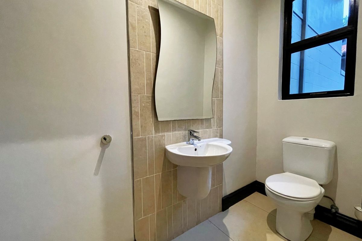 A clean and functional guest bathroom featuring a wall-mounted pedestal basin, a modern mirror, and a standard toilet.