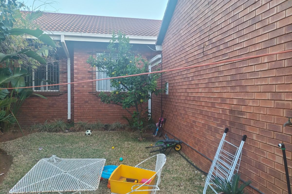 A rear exterior view of the townhouse featuring a brick facade, tiled roof, and a small garden area with established trees.