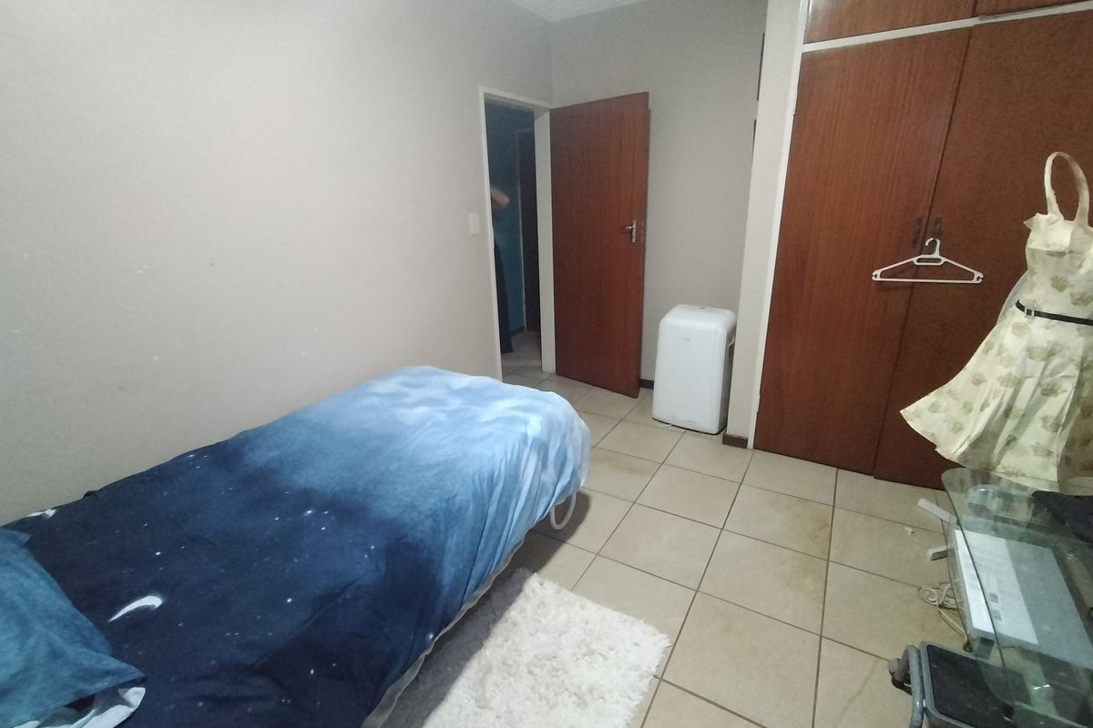 A bedroom featuring tiled flooring, built-in wooden cupboards, and neutral wall finishes, offering a functional space with potential for cosmetic updates.