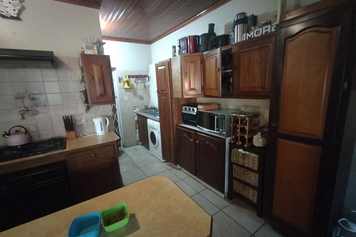 A dated kitchen featuring wooden cabinetry, a gas hob with extractor, tiled splashbacks, and a timber ceiling, with an integrated laundry area.